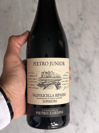 Zoom over a Zardini Valpolicella Ripasso Classico Superiore bottle of wine being held over light gray background